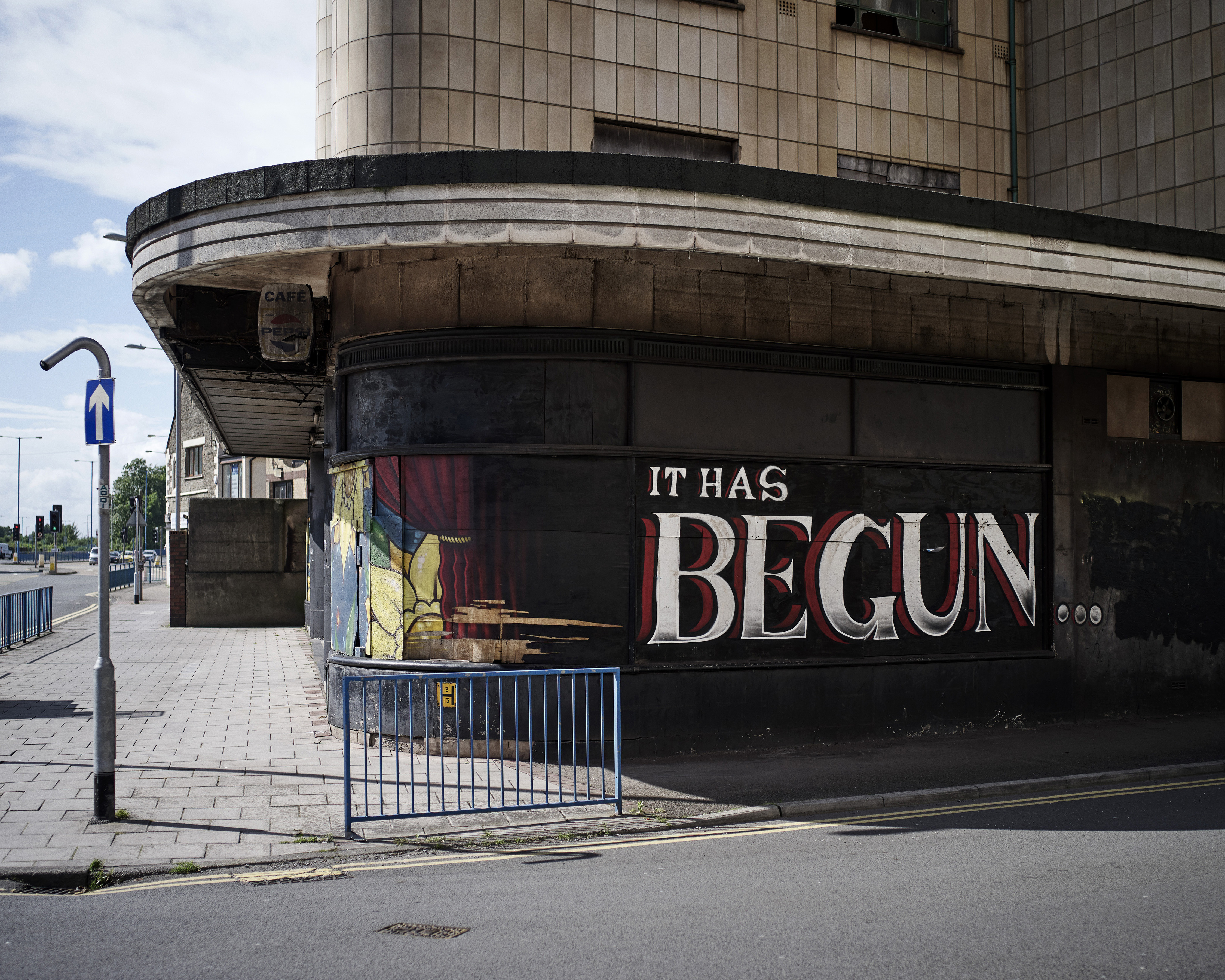 Building facade with the phrase "IT HAS BEGUN" painted in white and red, from the series Home, Sweet Home, by Ed Alcock.