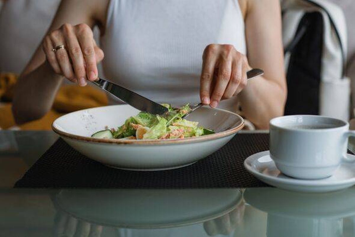 Close-up of a young woman sitting at a table eating a salmon and quail egg salad with a black coffee