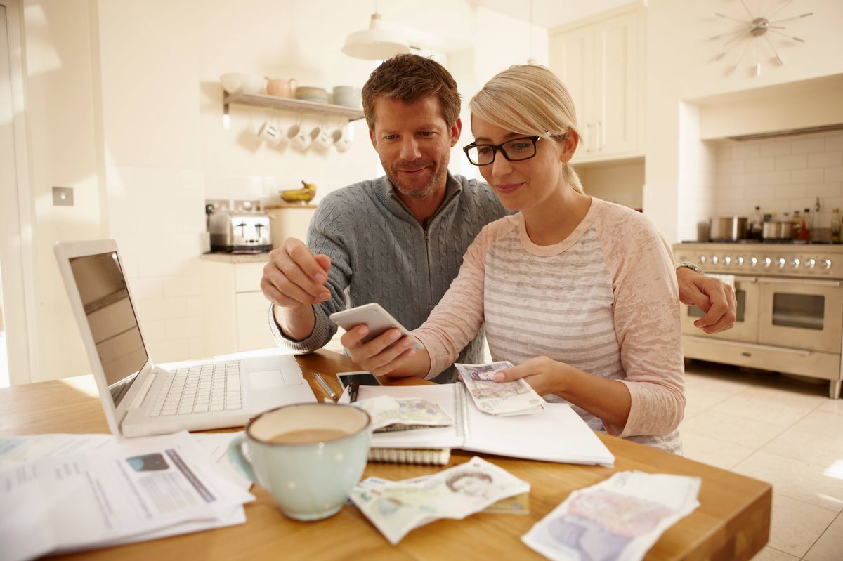 Couple going through finances together, sitting by table with computer and spreadsheets