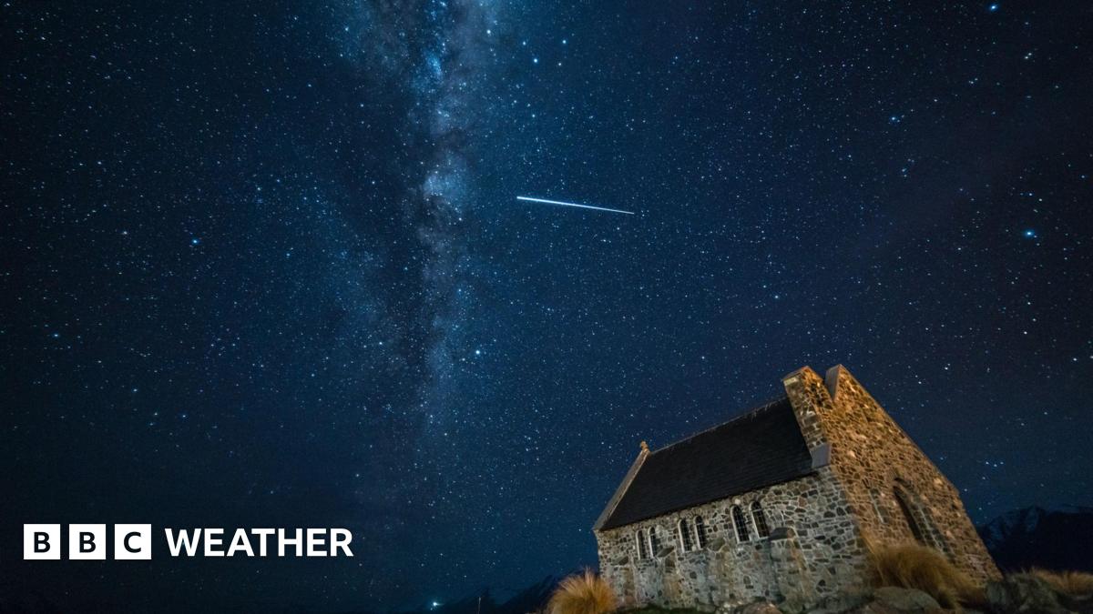 Streak of light in star-filled dark night sky above a church