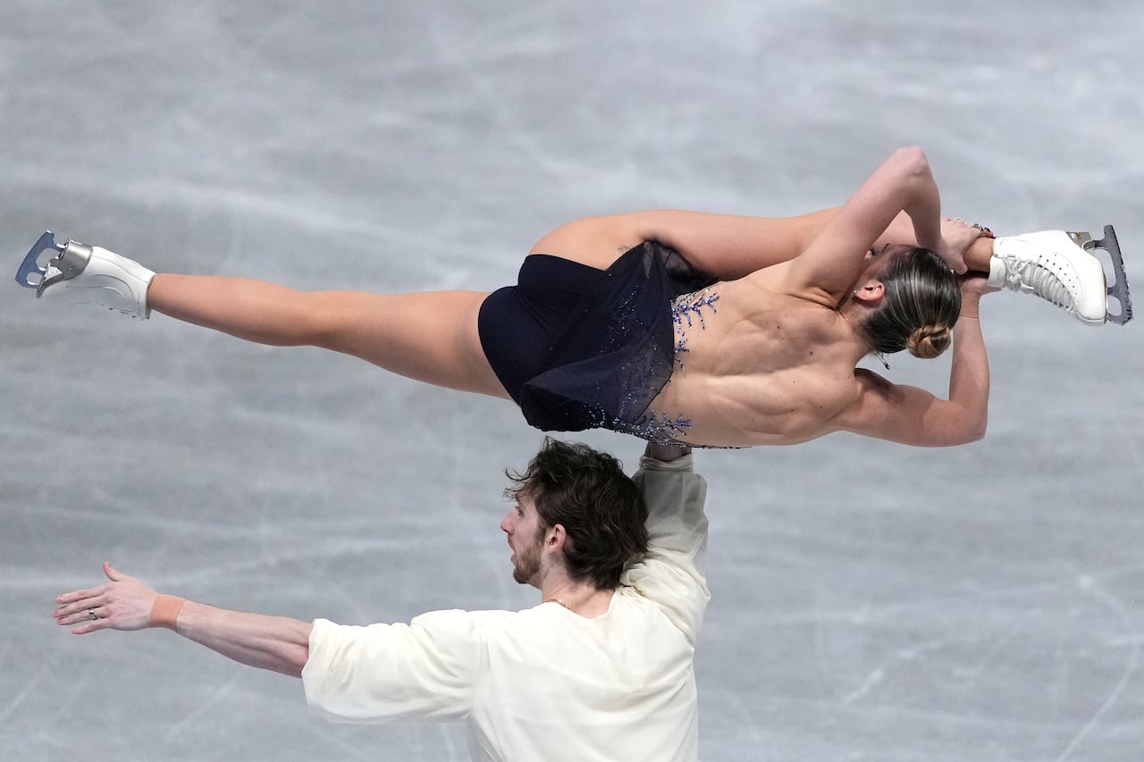 A pair of ice skaters, with female doing splits sideways while her partner holds her torso.