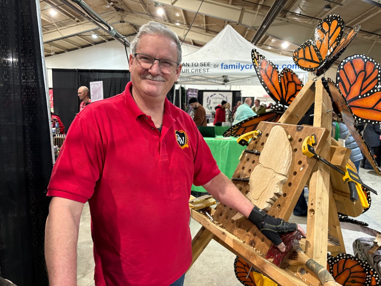 A white man with white hair and a white moustache. He wears glasses and is in a red t-shirt.