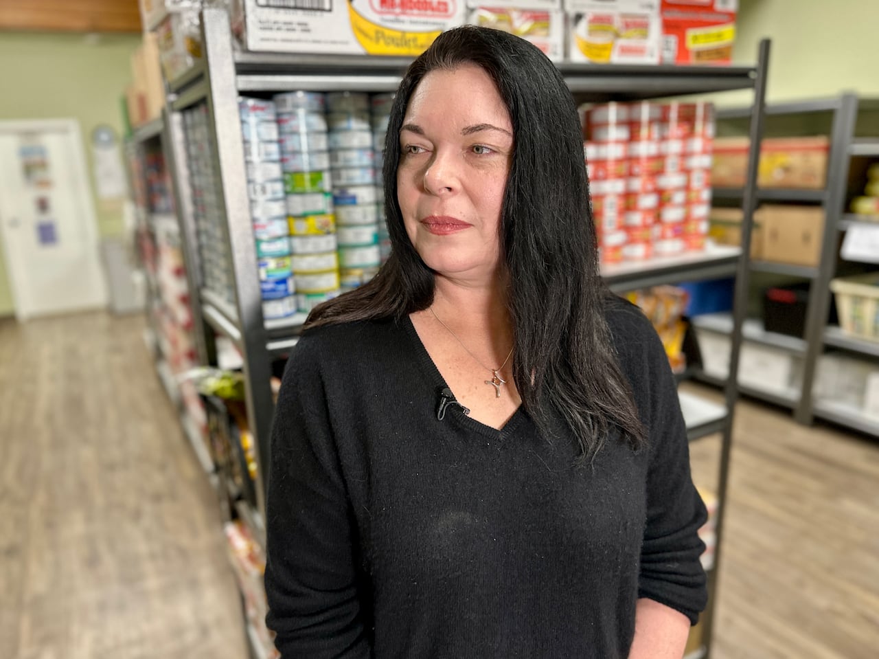 A woman in a black shirt starts inside a food bank with non-perishables lining the shelves.