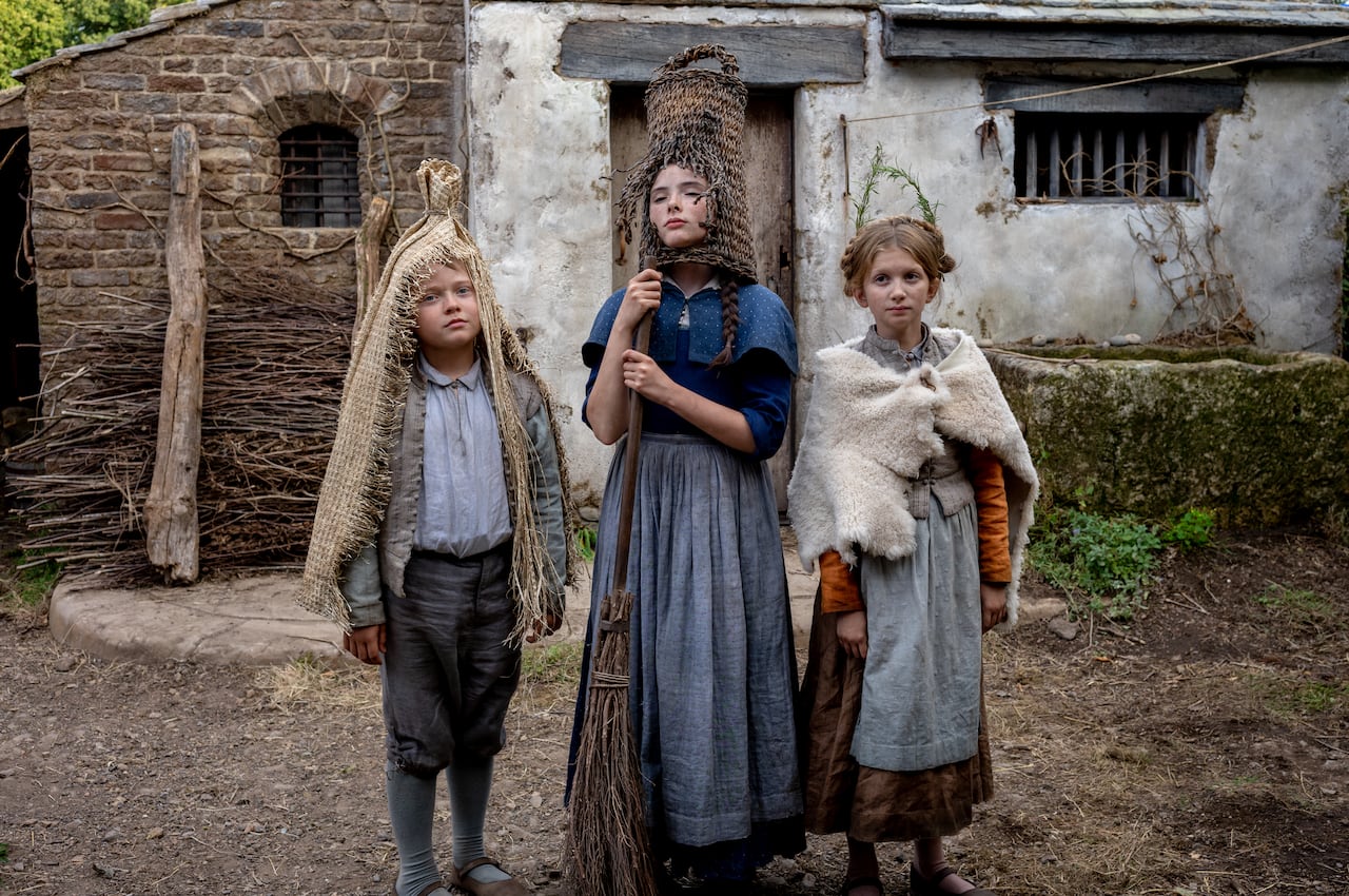 Three children in period-dress pose in a garden.