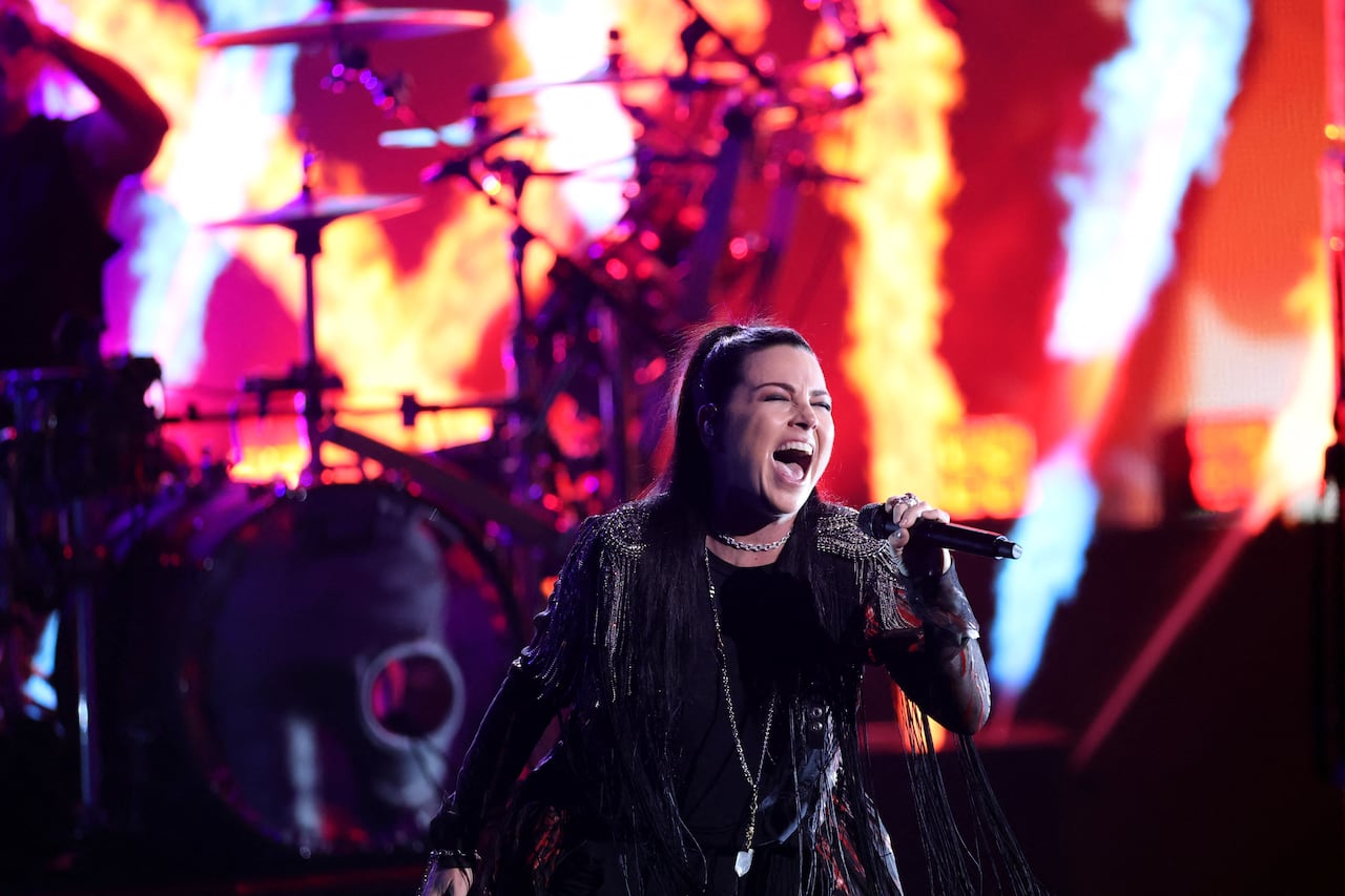 a woman in a black gothic outfit screams into a microphone on stage, with her band in the background
