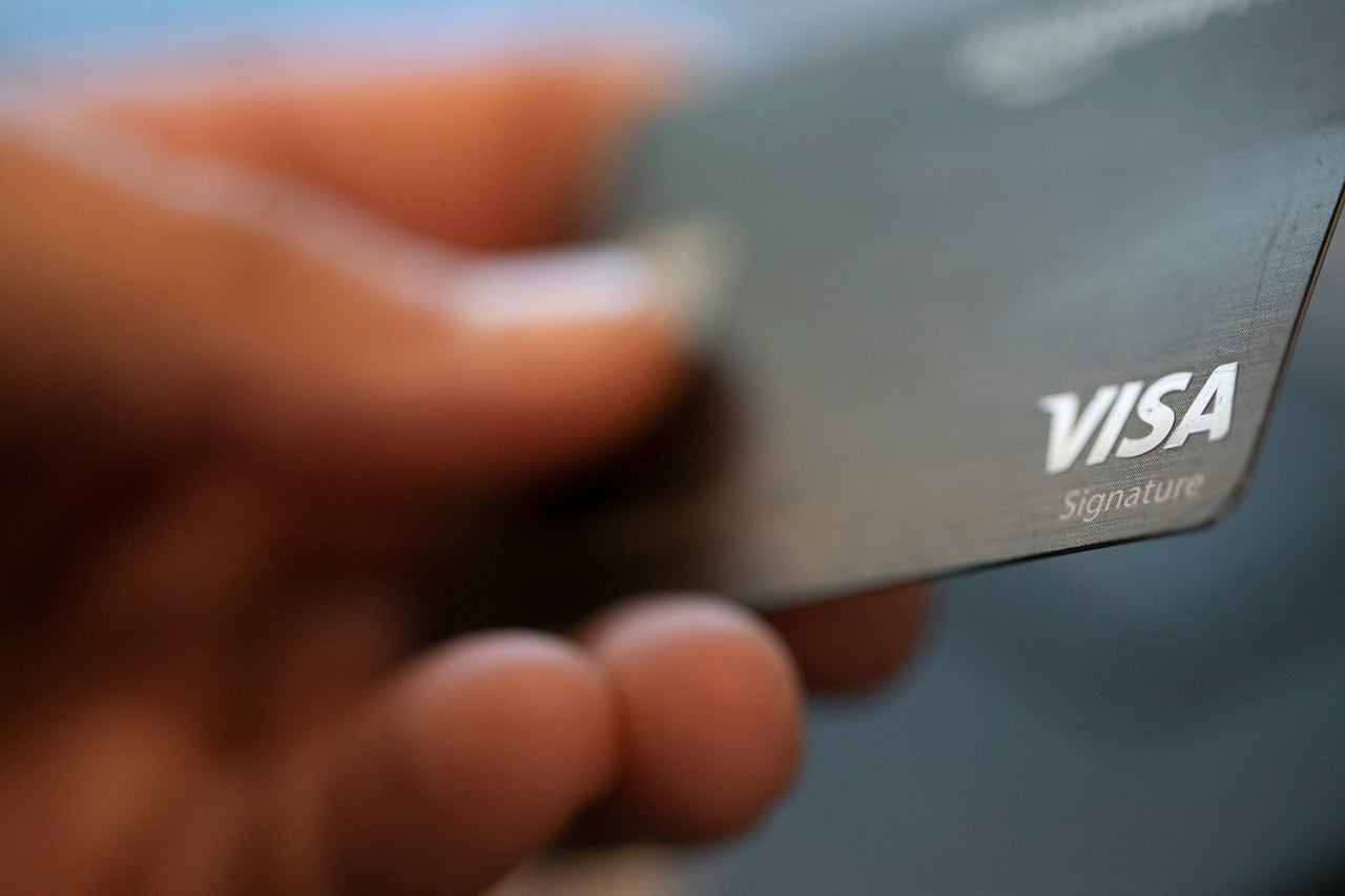 A person holds a black, Visa credit card in close-up.
