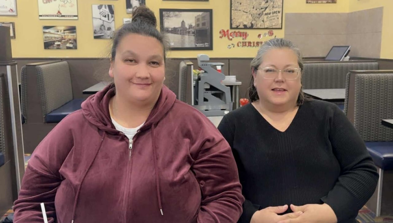 A woman and her aunt are seen sitting in a restaurant and smiling to the camera.