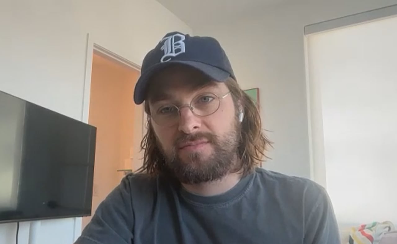 Man with glasses and cap sitting in front of TV