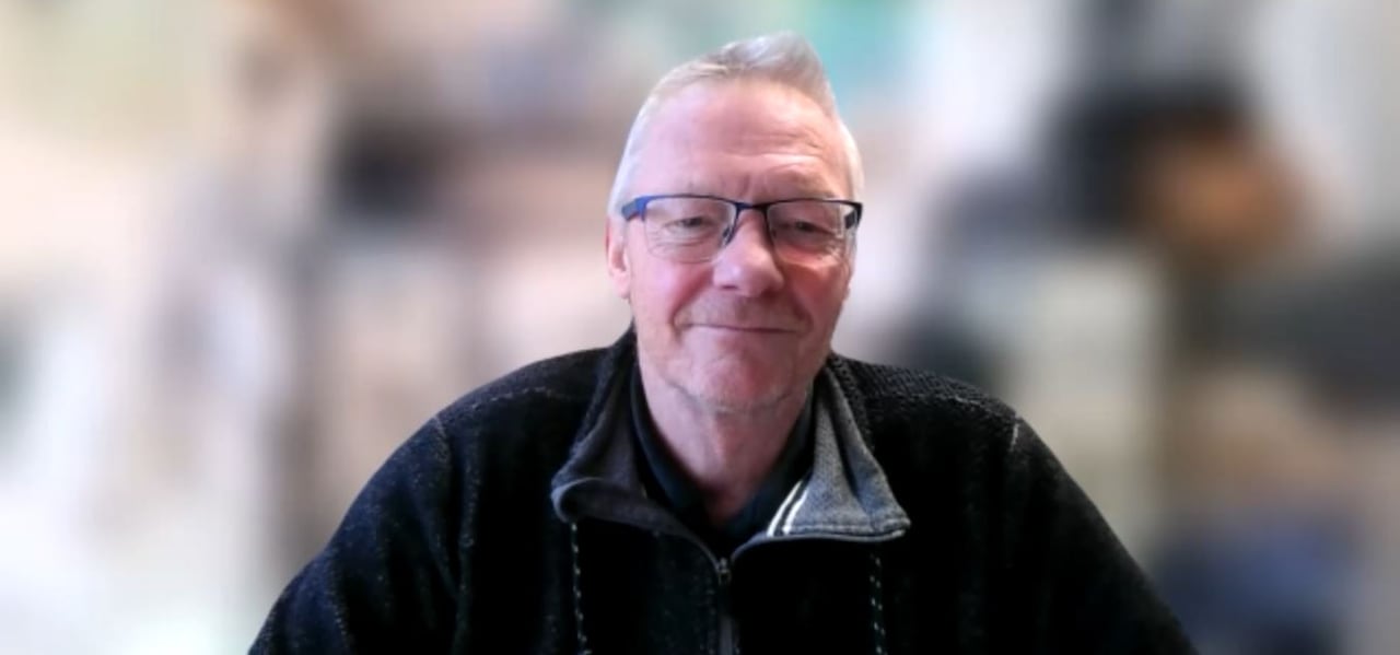 A man with white hair wearing a dark blue sweater and glasses