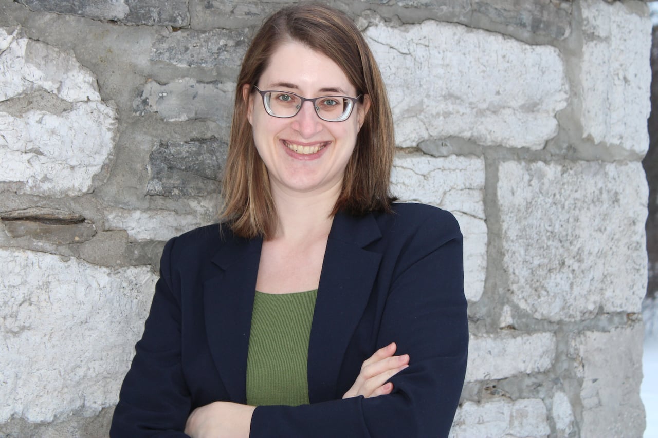 A woman with glasses in a blazer against a brick wall. 