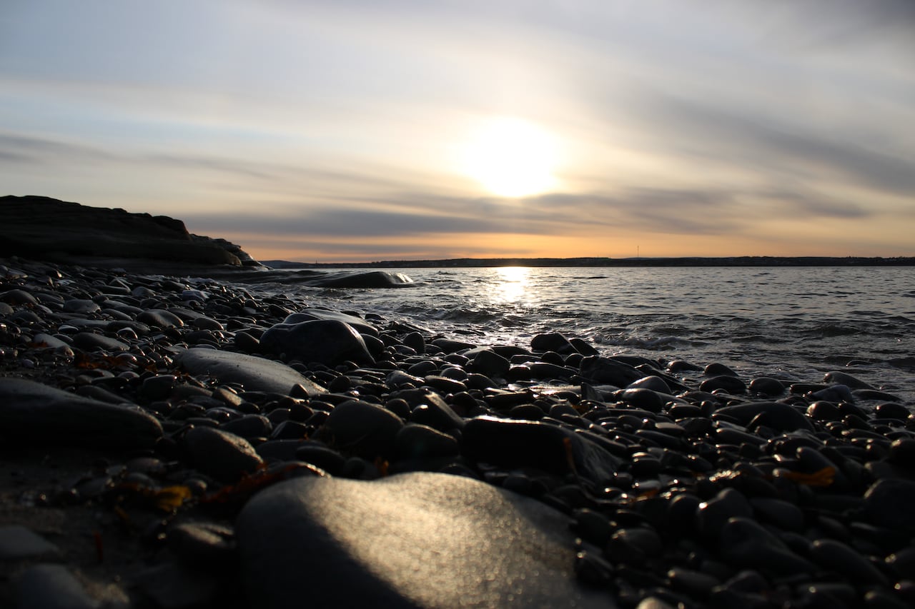 up close photo of rocks on a beach at dusk with the sun going down in the distance