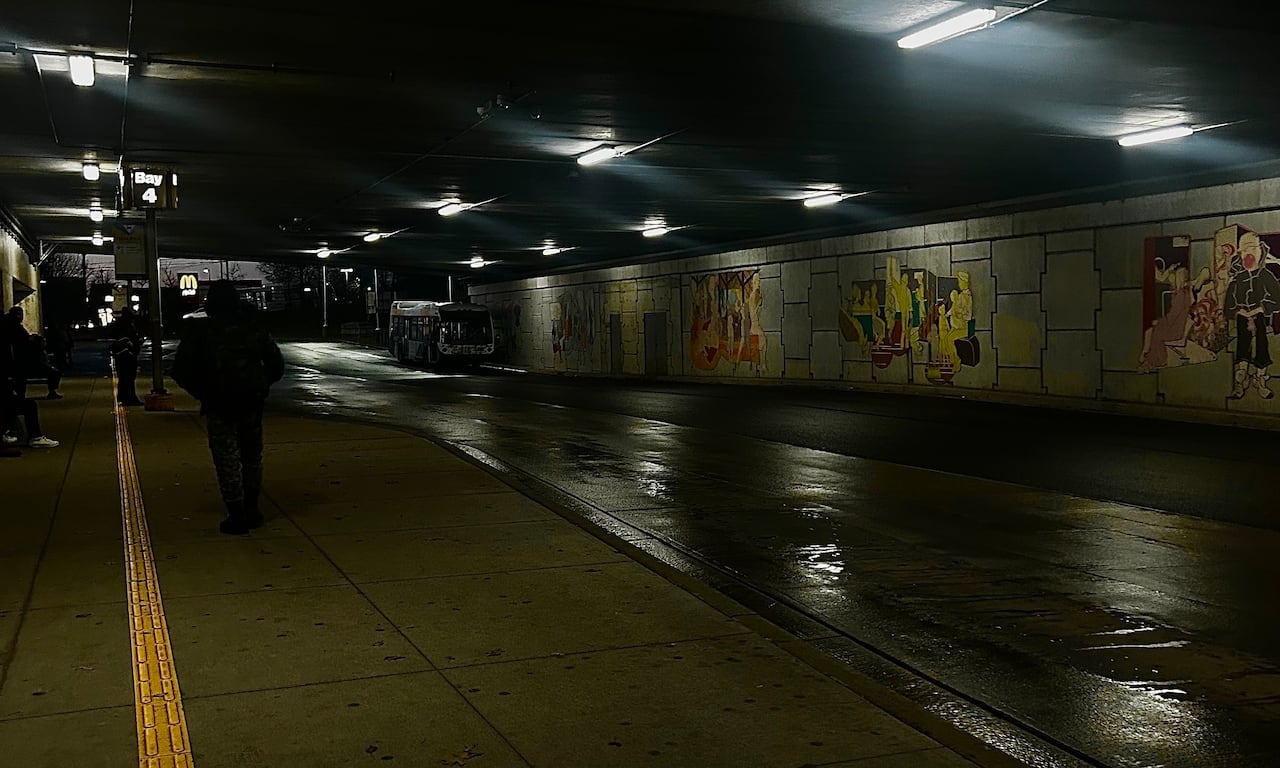 shadowed person walking down rainy sidewalk inside a bus terminal