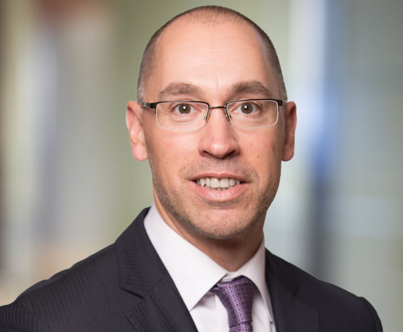 A man with glasses wearing a suit and tie seen in a formal headshot 