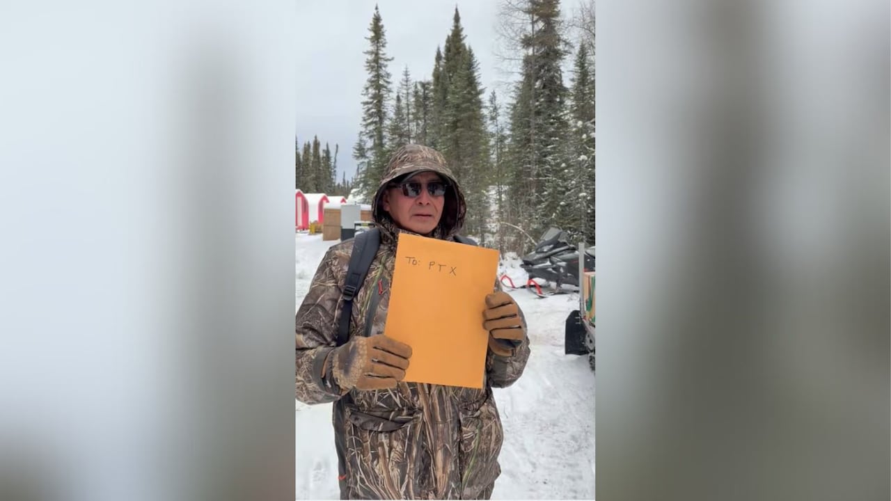 A person wearing a camouflage-patterned coat is seen holding an envelope with "PTX" written on the outside.