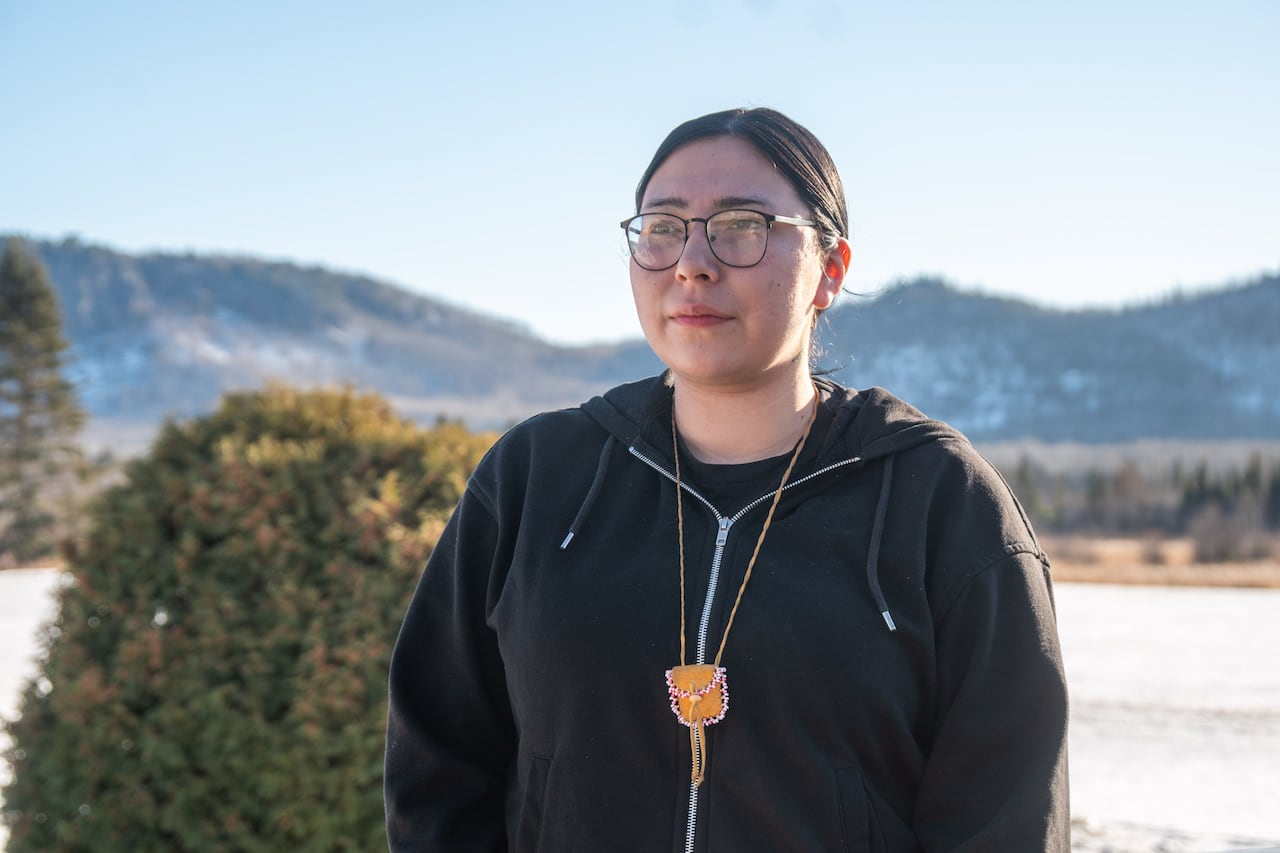 A person wearing glasses and a dark-coloured hoodie is seen standing outside in a snowy place.