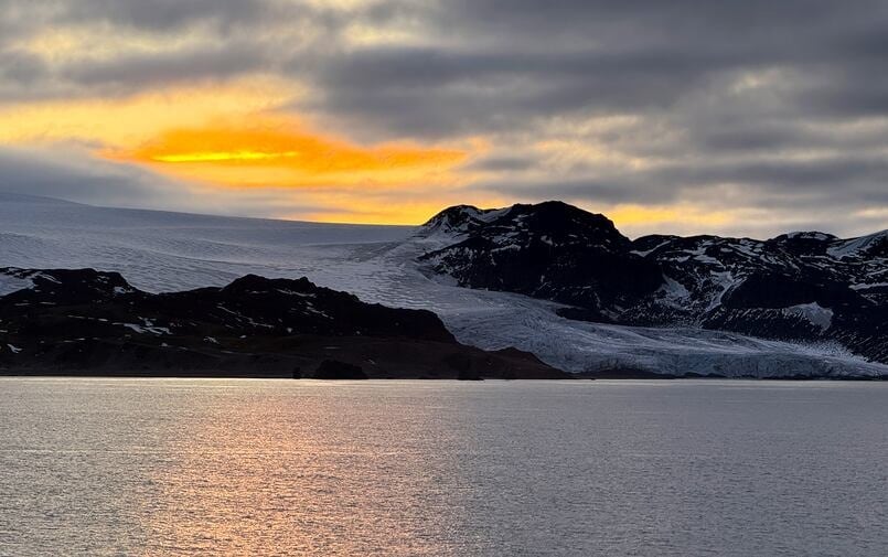 sun sets behind mountains, with ocean in foreground
