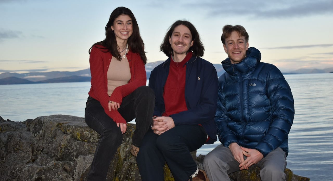 A group of three young people smile next to an ocean.