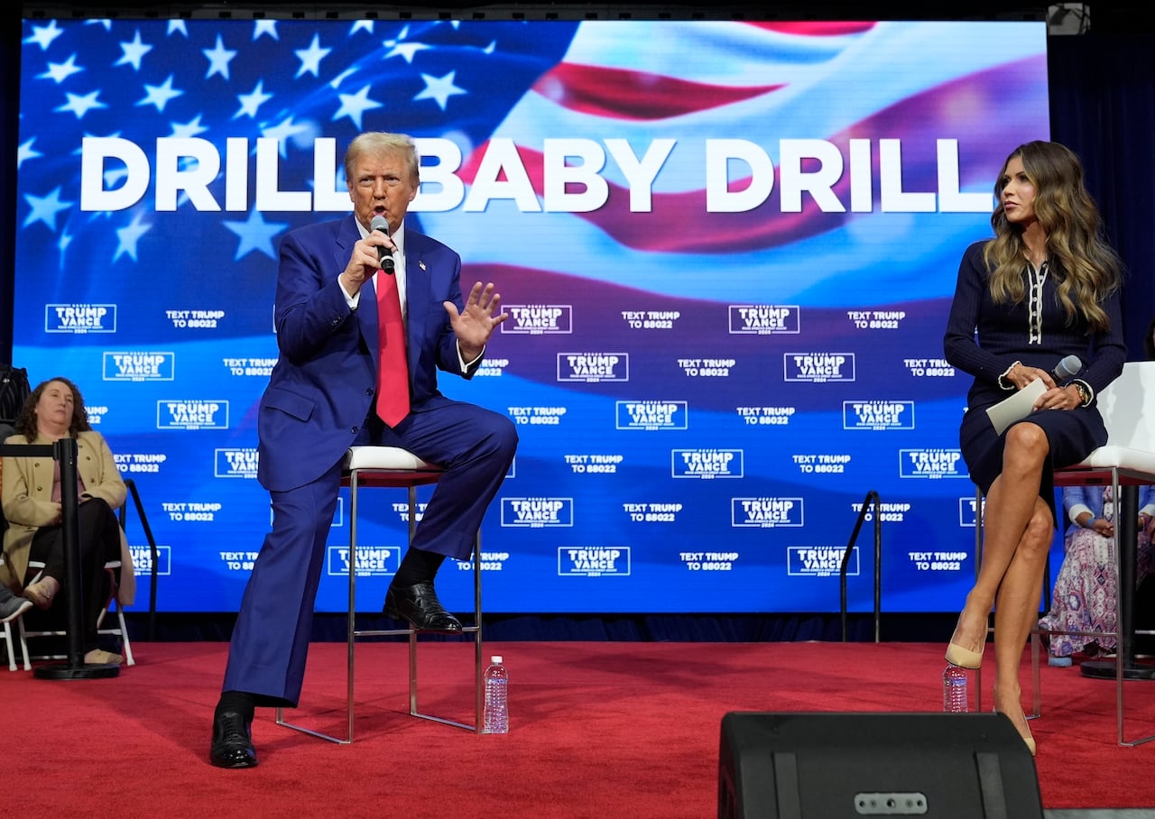 A man speaks in front of a screen reading 'Drill, Baby, Drill' as a woman looks on.
