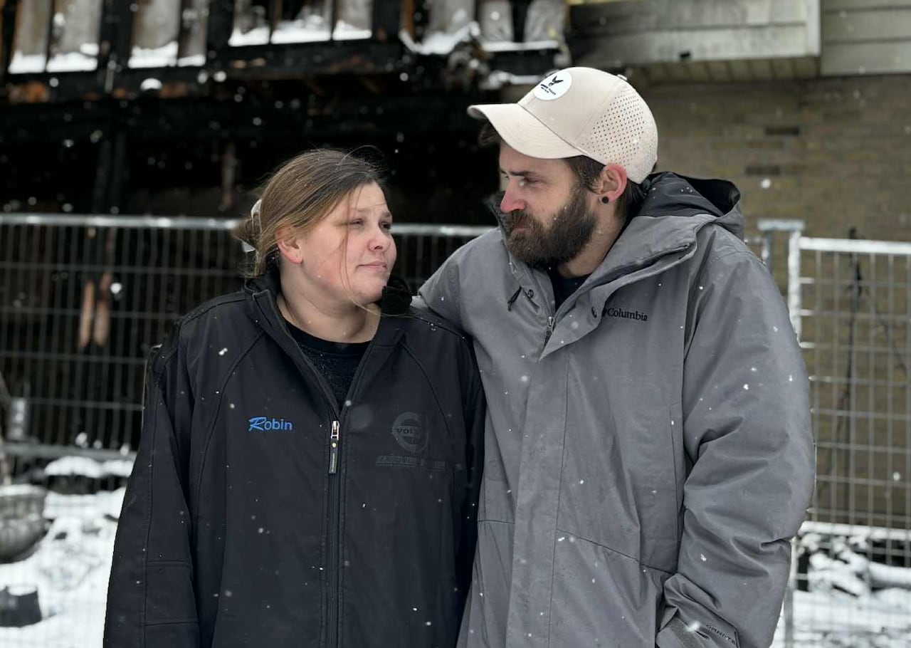 Two people look at each other while standing in front of a burnt townhouse