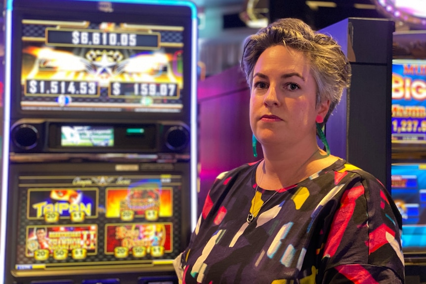 Woman with stylish short grey hair wearing colourful clothes standing in front of pokies