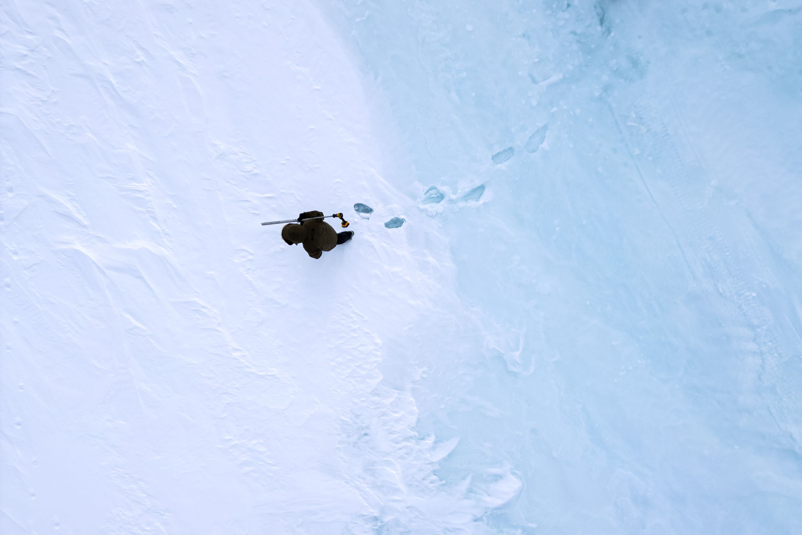 A photo from above of a person walking where ice meats the snow