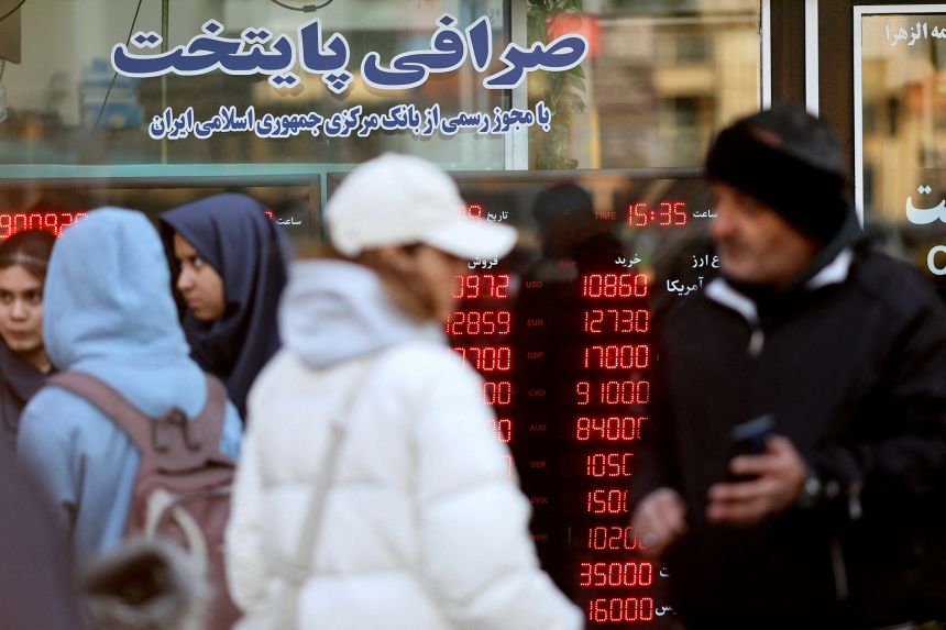 People walk past a display sign at a currency exchange bureau as the value of the Iranian rial drops, in Tehran, Iran, December 20, 2025.