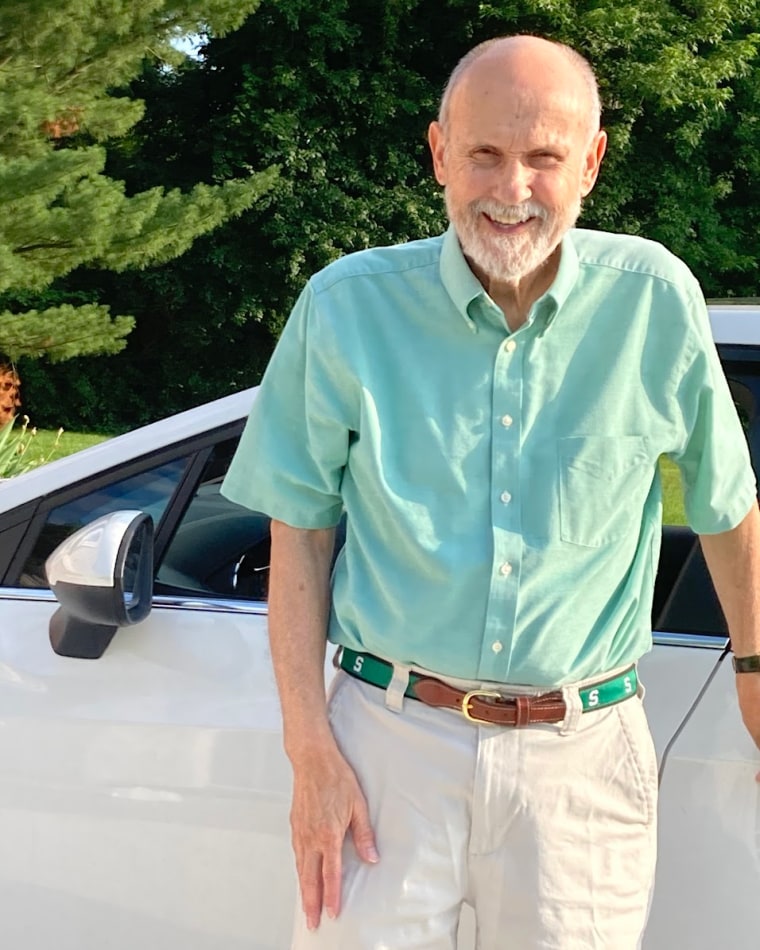 Tom Howie smiles while standing on the side of a car outside
