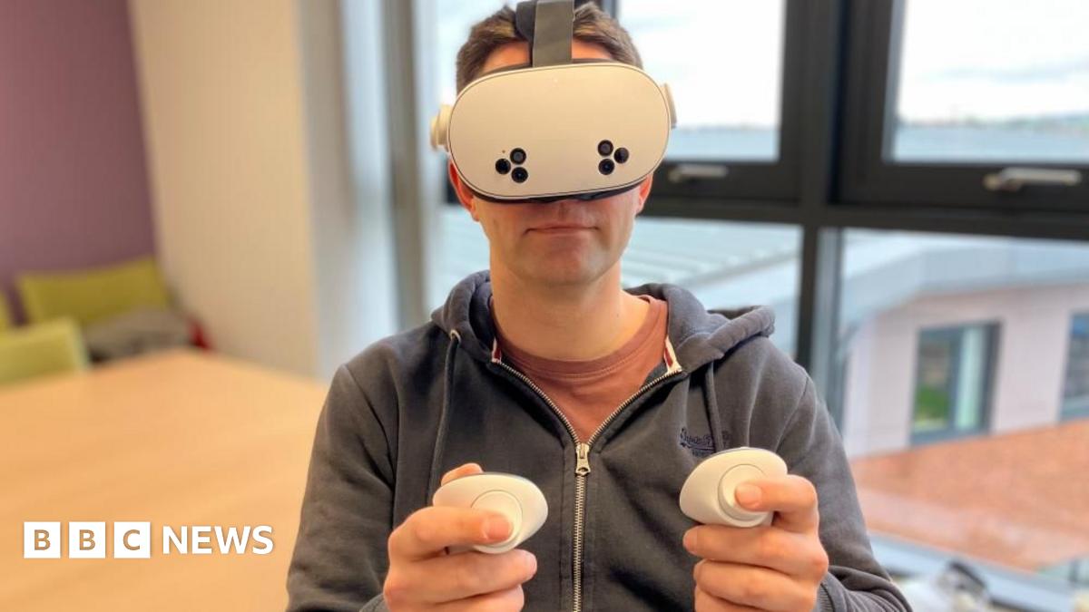A man with short brown hair and glasses sits in a meeting room and smiles at the camera.