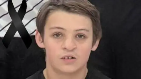 SCOCS - Basquetebol An image of Alfie Hallett who is wearing a black basketball uniform and is looking directly at the camera