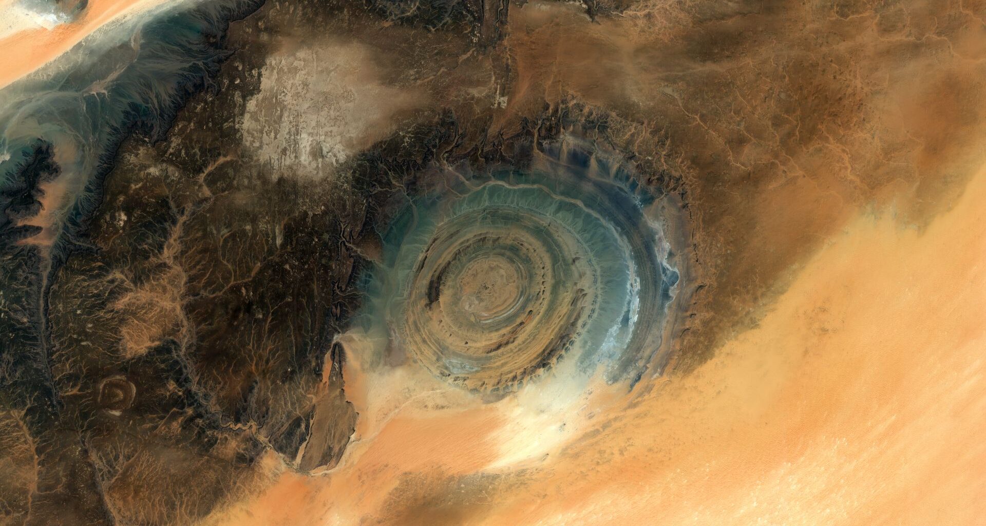 A dark circular eye peers out of a lighter landscape of the Saharan Desert