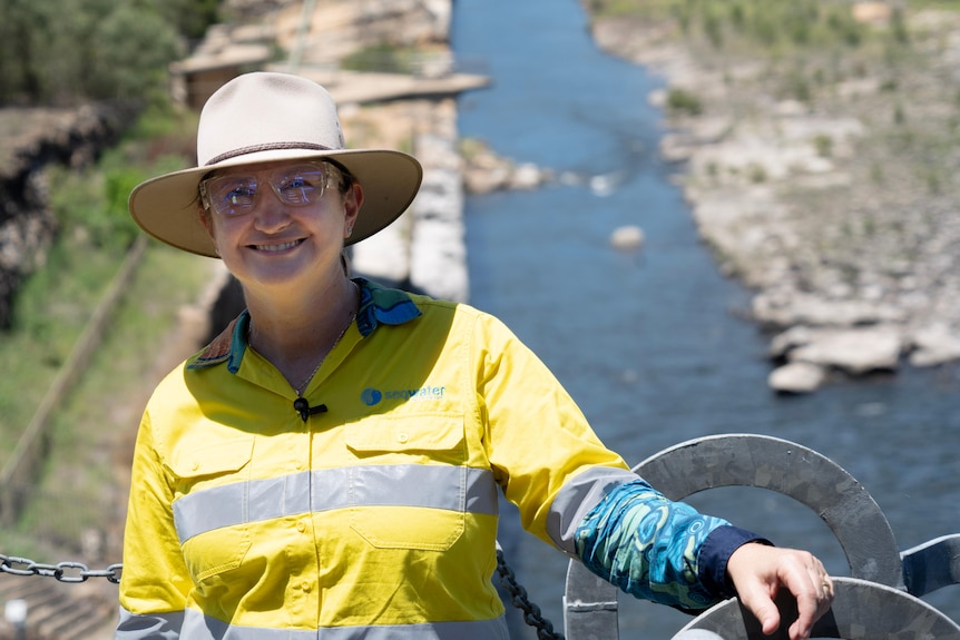 A woman in broad brim hat and hi-vis workwear and safety goggles smiling at the camera