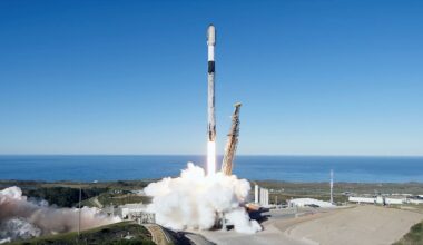 a white rocket with a black interstage lifts off from its oceanside launch pad into a clear blue sky