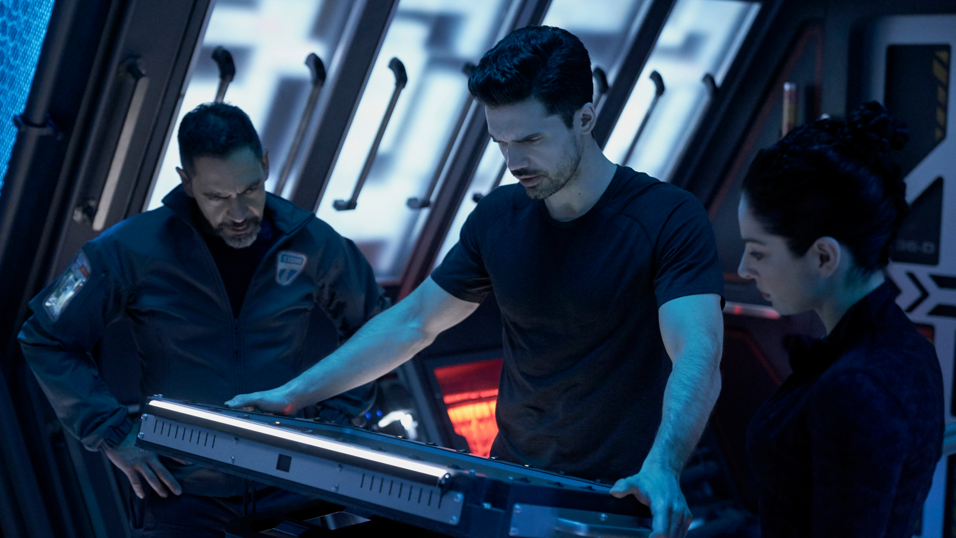 Three people looking at a sci-fi workstation aboard a spaceship in The Expanse.
