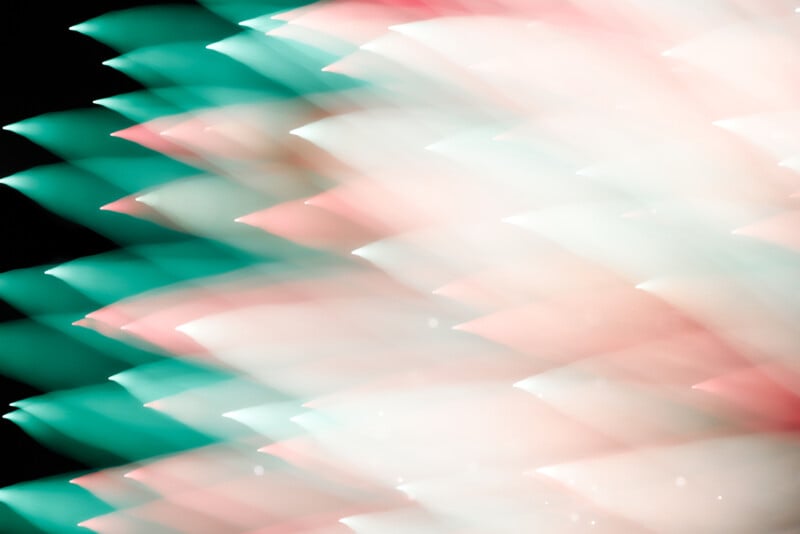 Abstract image featuring layered, blurred shapes in green, pink, and white tones, creating a dynamic, wave-like pattern against a black background. The colors blend softly, giving a sense of motion and lightness.