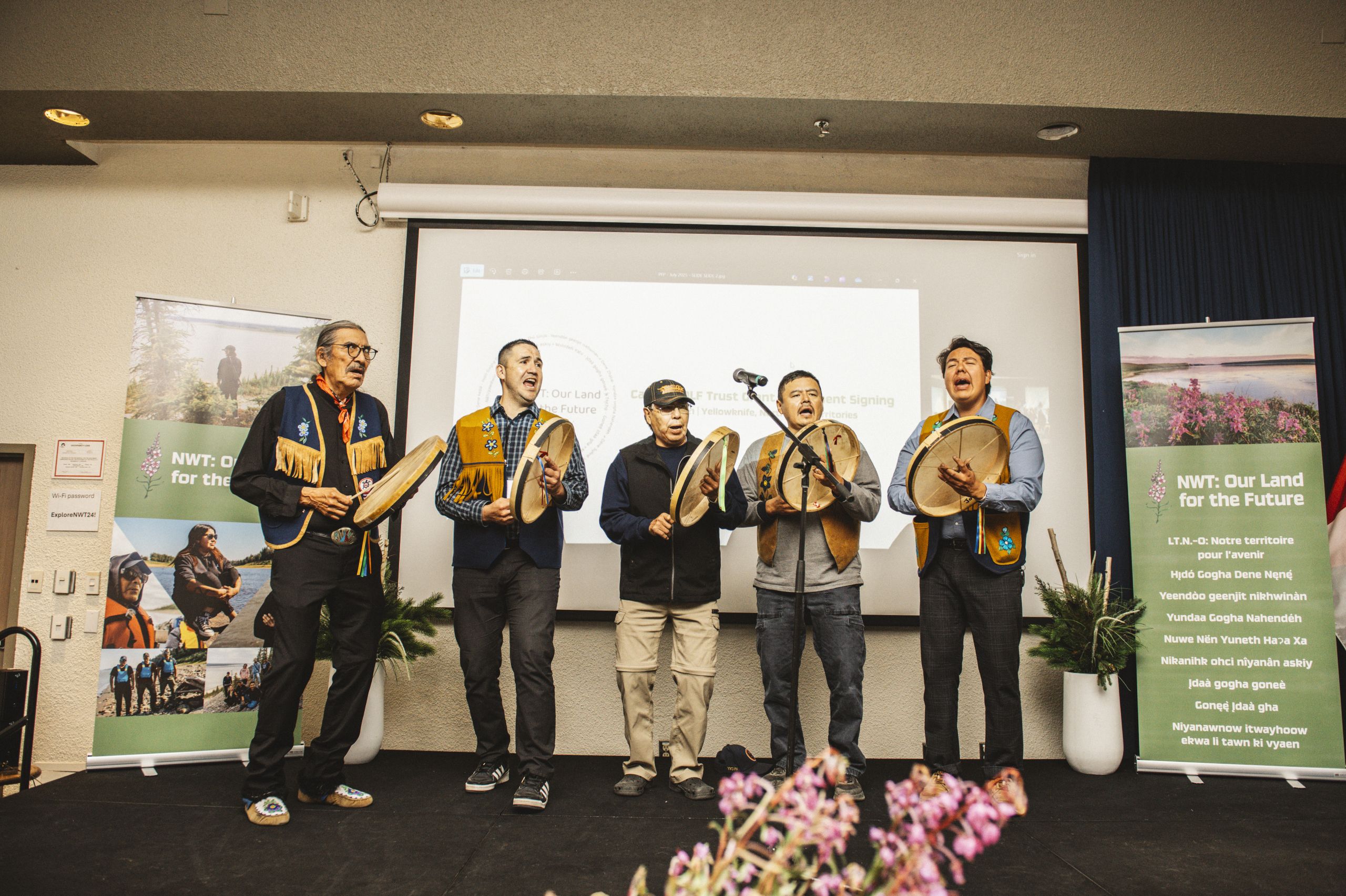 Five people sing and play rawhide drums on a stage