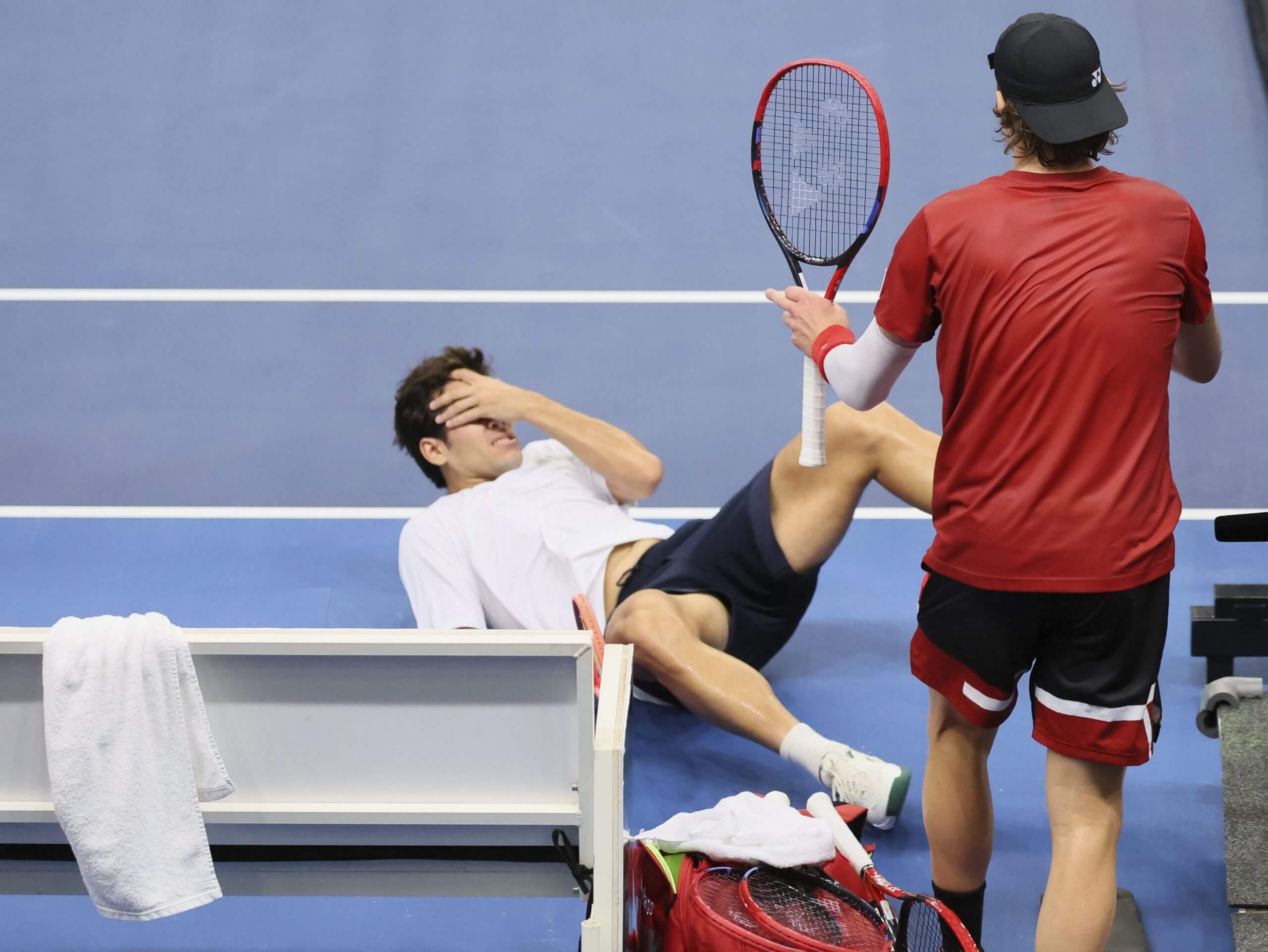 Cristian Garín on the floor holding his face as Zizou Bergs stands over him with his left hand raised in apology holding his tennis racket.