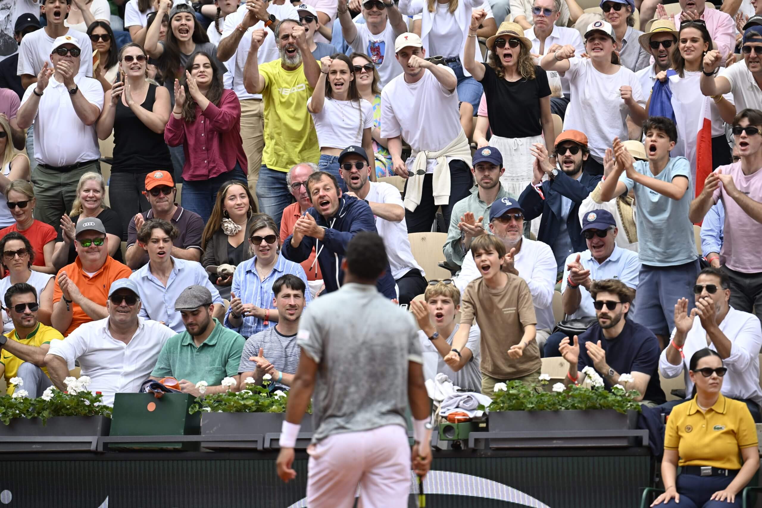 Fans in the stands roar in front of Arthur Fils, who has his back to the camera.