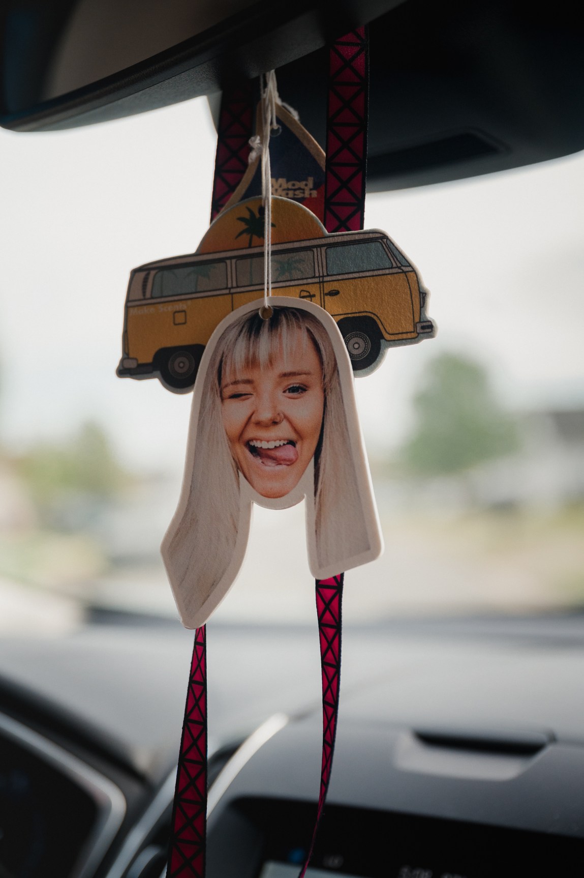 A cut out photo of a blond woman sticking out her tongue hangs from a rearview mirror.