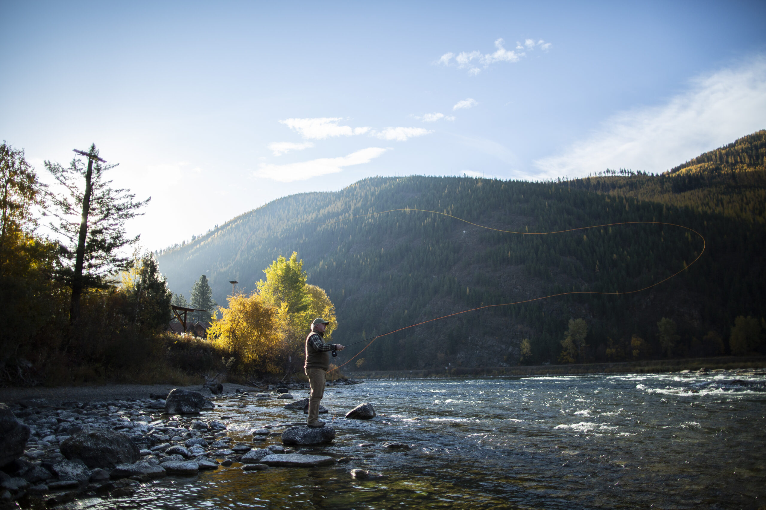 A fly fisherman casts a line over a picturesque river with shallow rapids