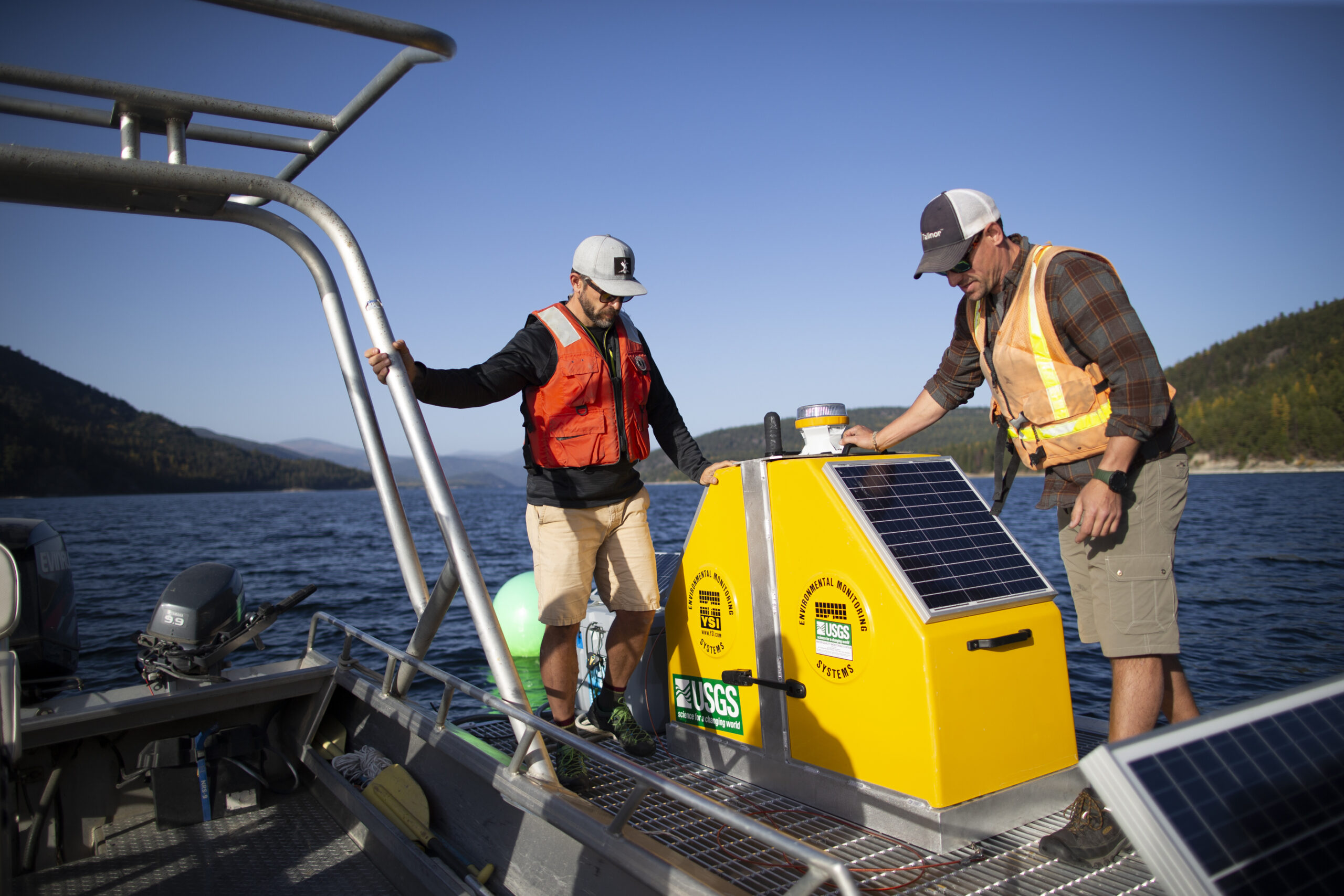 Two men in orange vests walk on a boat out on the water