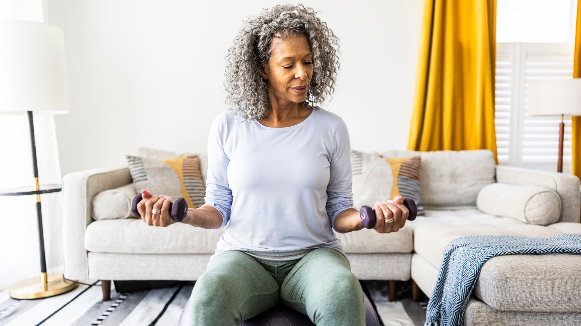 senior woman sits on exercise ball and does light weight exercises