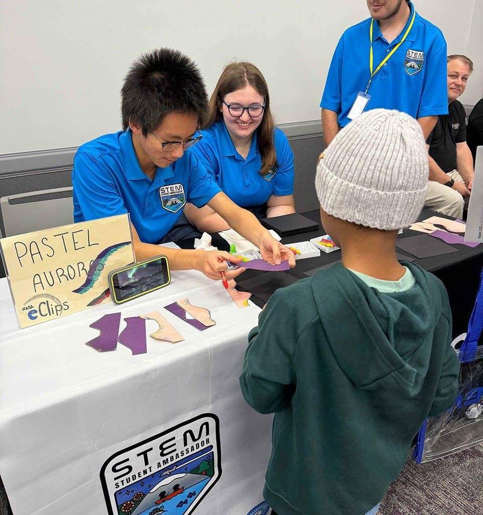 STEM Ambassadors assist a young boy in making a pastel aurora.
