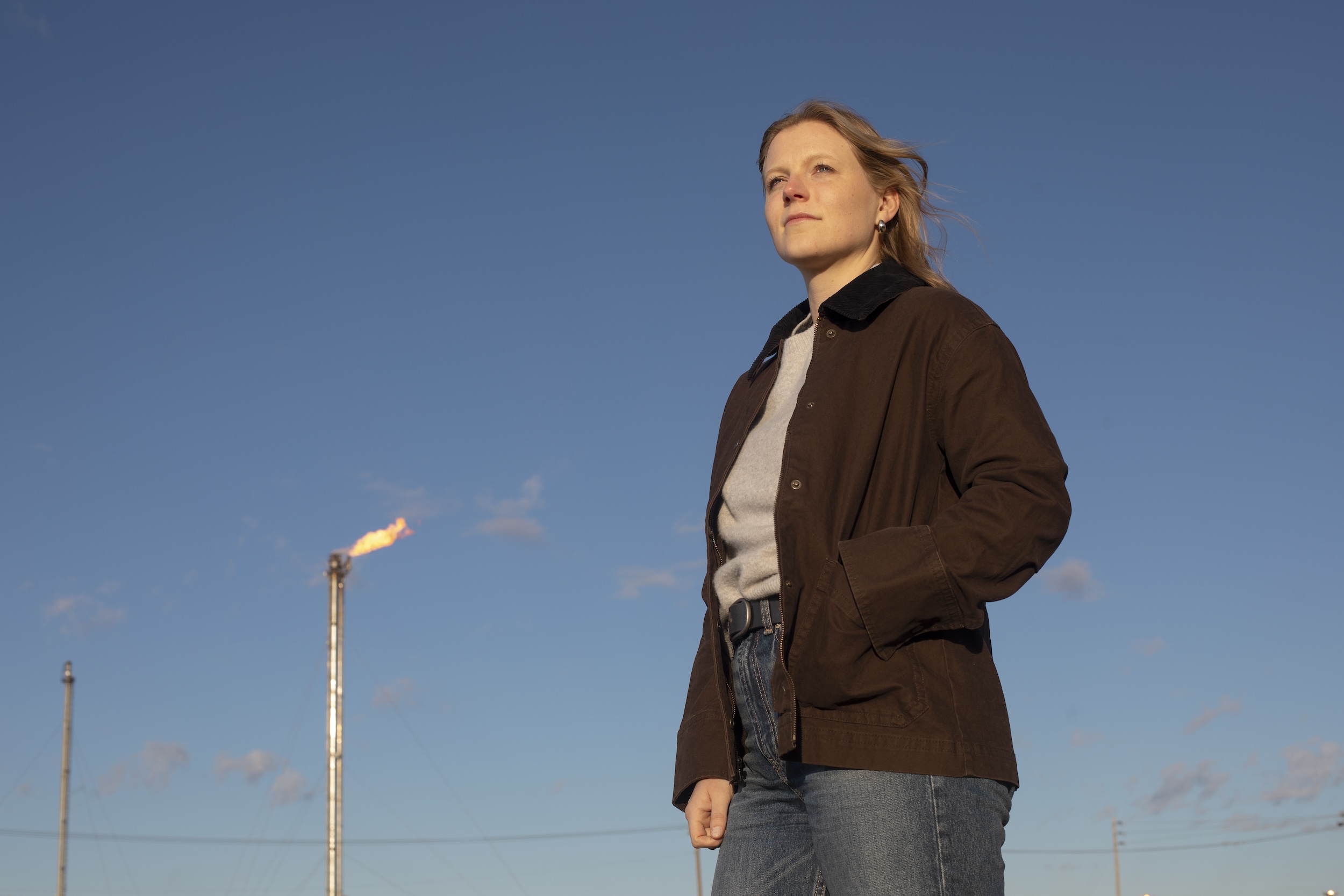 Dr. Julia Sawatzky in front of a flare stack at an Alberta refinery in 2025. Her hand is in her pocket and she is looking up and away from the camera.