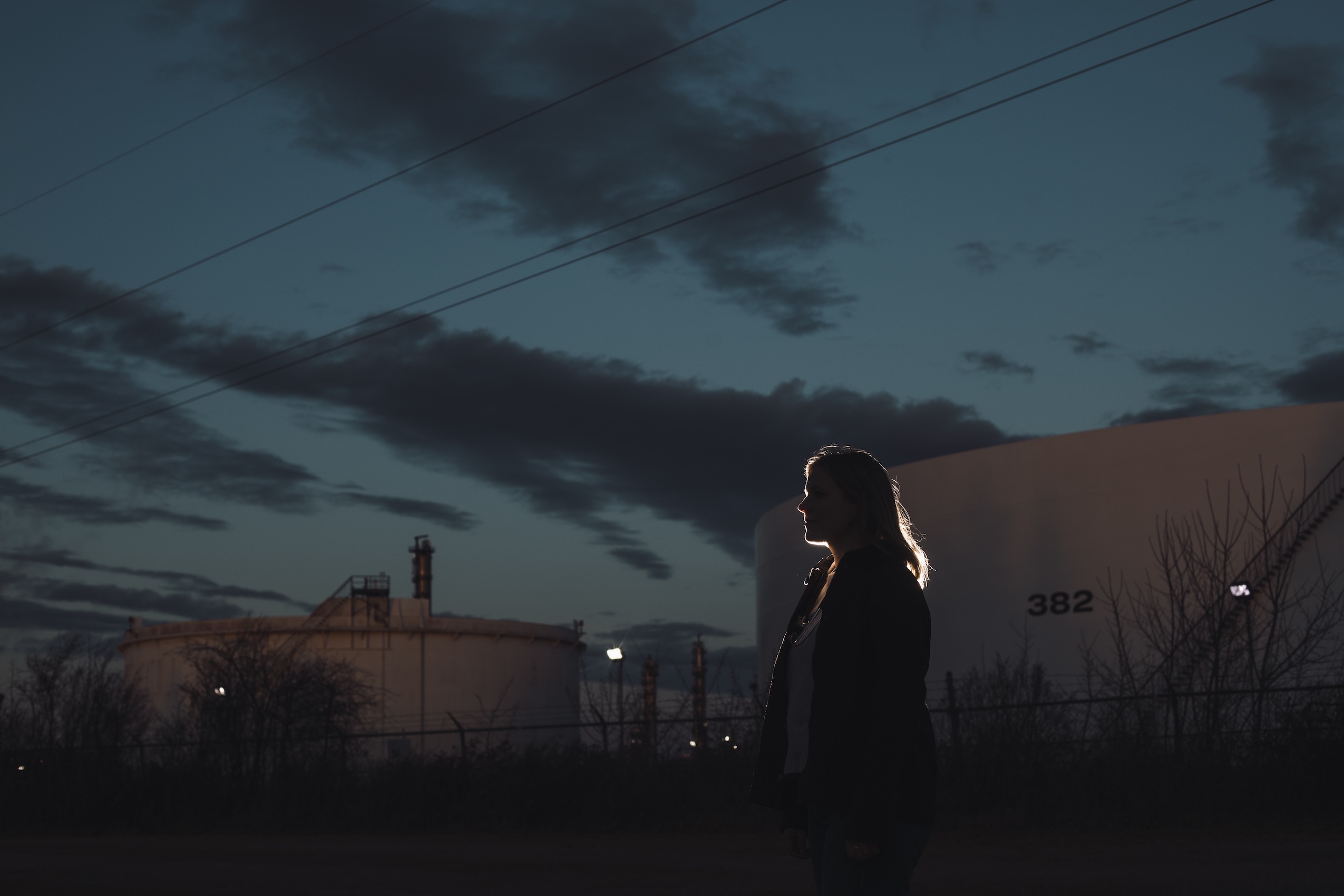 A woman stands in the fading light of dusk, her silhouette outlined by light.