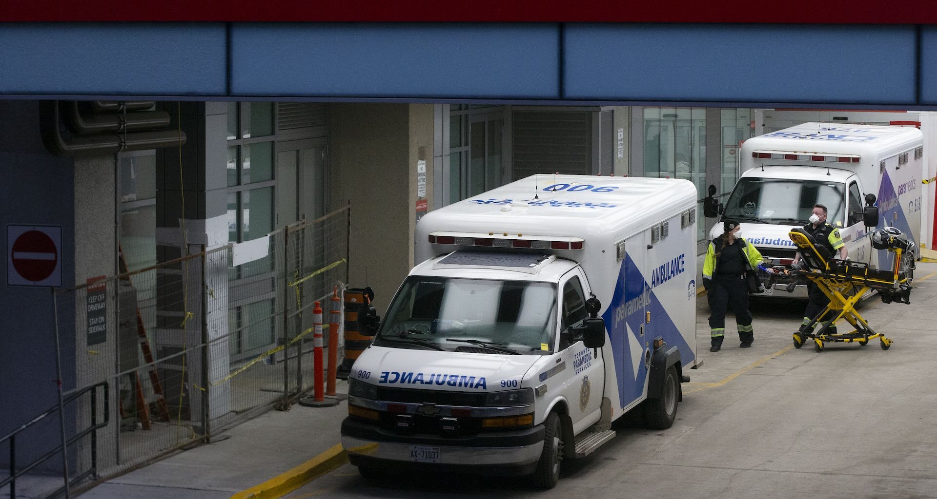 Paramedics moving equipment at an emergency room entrance. There are two ambulances parked by the entrance.
