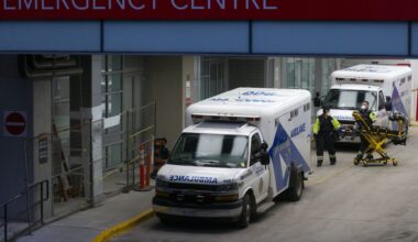 Paramedics moving equipment at an emergency room entrance. There are two ambulances parked by the entrance.