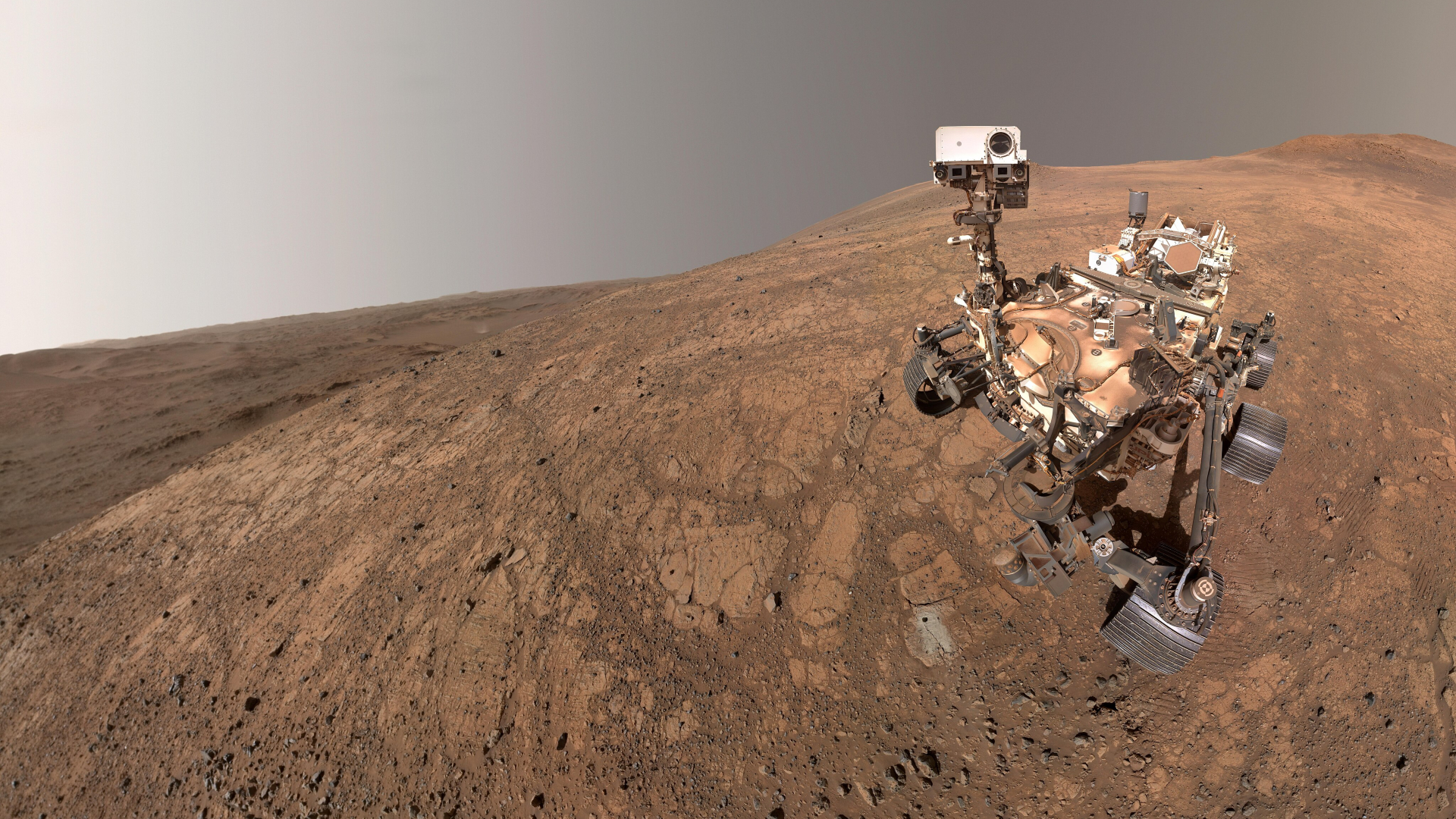 A rover sits on the reddish brownish surface of Mars