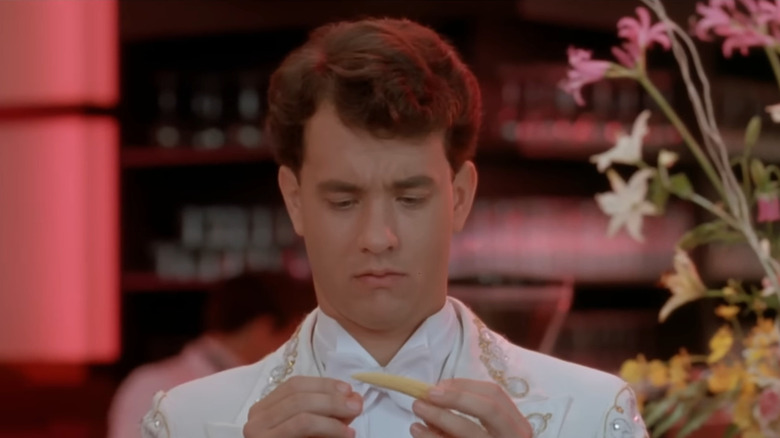 Tom Hanks as Josh in white suit looking down at baby corn in Big