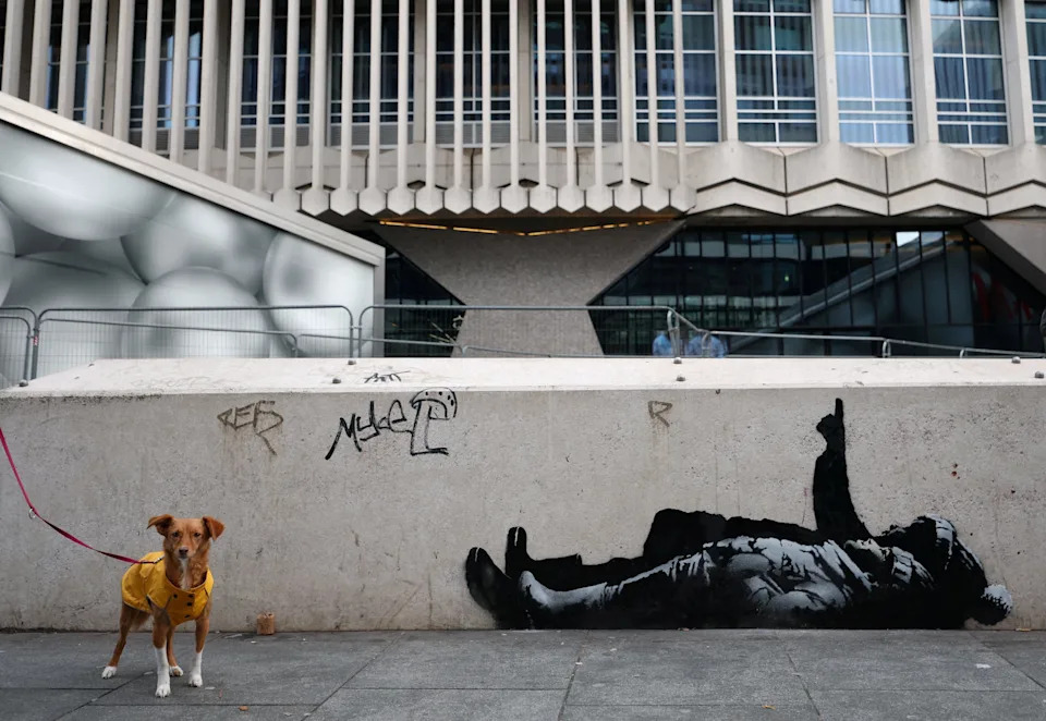 A dog stands beside a new mural reported to be by anonymous artist Banksy, in Tottenham Court Road, London, Britain, December 22, 2025.
