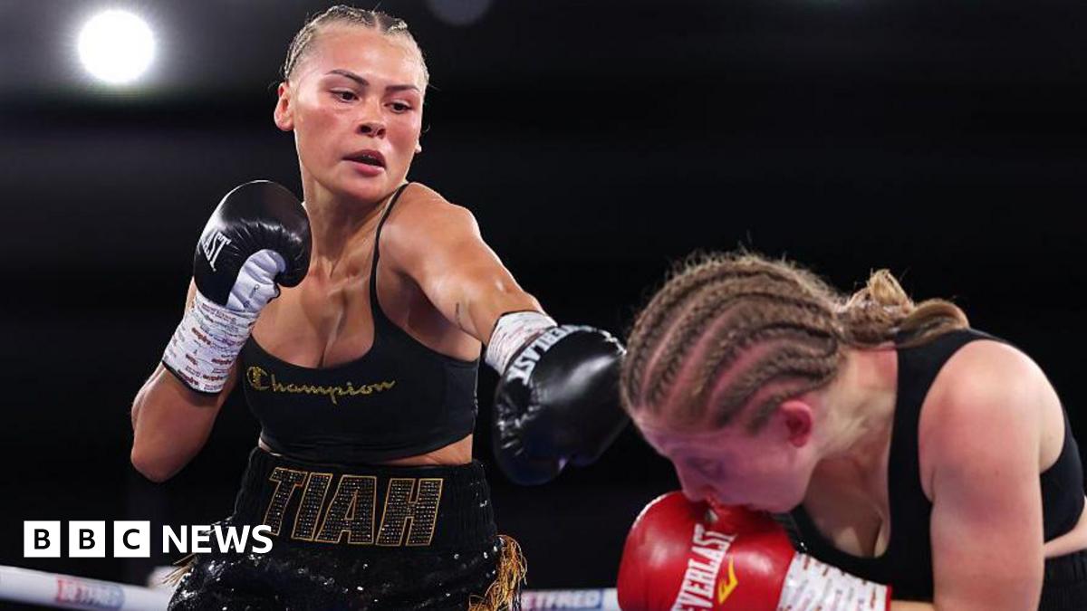 Tiah-Mai in the ring, she black boxing gloves on, black short and top, her hair is braided. The other boxer is wearing red gloves and is crouching down in the right hand side.